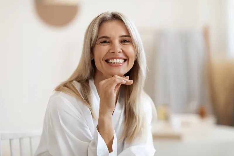 Mujer sonriente con blusa clara sentada en el interior.