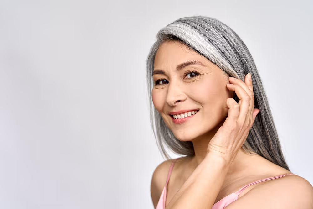 Smiling woman with silver hair touching face